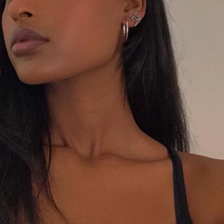 Side profile close-up of a woman with dark hair, showing her neck and jawline, wearing layered silver earrings and a black top.