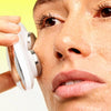 Close-up of a person using ZIIP HALO device on their cheek against a bright yellow and white background.